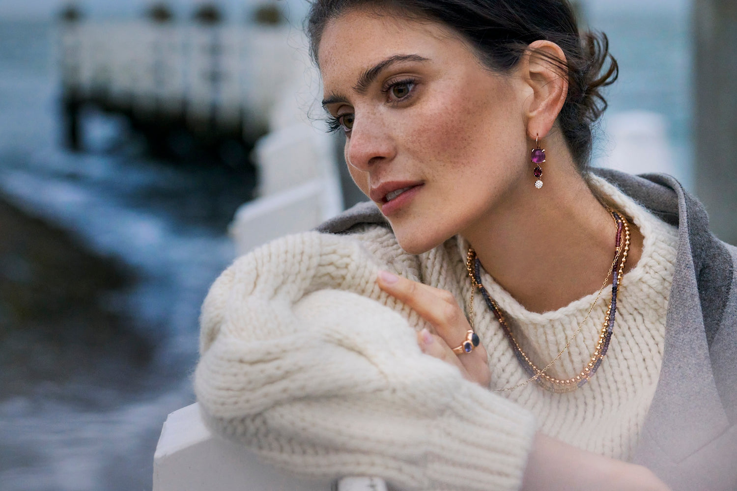 Frau in weißem Wollepullover und Schmuck schaut interessiert auf Wasser